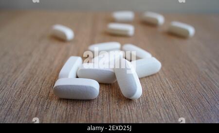 Haufen von Kalzium, Vitamin-Ergänzung Tabletten isoliert auf hölzernen Hintergrund. Viele medizinische weiße Pillen und Kapseln für starke Knochen. Bleib sicher und gesund Stockfoto