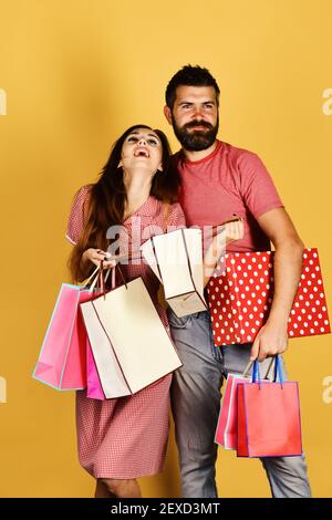 Paar in der Liebe hält Einkaufstaschen auf gelben Hintergrund. Shopping und Ausgaben Konzept. Mann mit Bart hält Red polka gestrichelten Kasten. Kerl mit Bart und Mädchen mit glücklichen Gesichtern einkaufen. Stockfoto