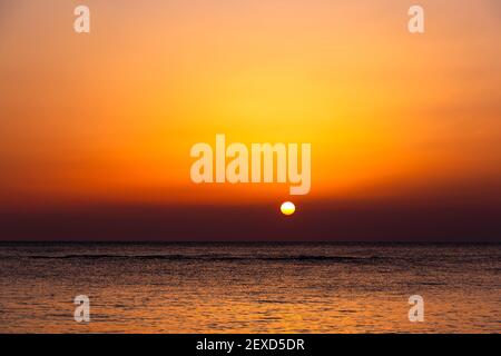 Heller Sonnenuntergang mit einer großen gelben Sonne unter der Meeresoberfläche. Stockfoto