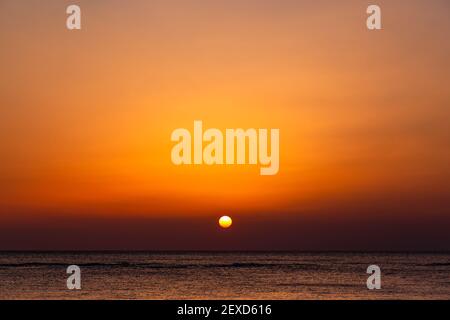 Heller Sonnenuntergang mit einer großen gelben Sonne unter der Meeresoberfläche. Stockfoto