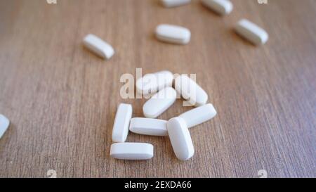 Haufen von Kalzium, Vitamin-Ergänzung Tabletten isoliert auf hölzernen Hintergrund. Viele medizinische weiße Pillen und Kapseln für starke Knochen. Bleib sicher und gesund Stockfoto