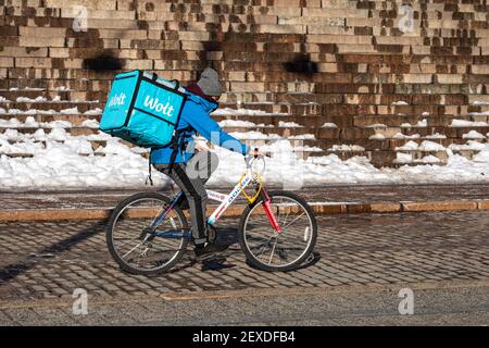 Wolt Food Delivery Kurier mit Thermalrucksack radeln vorbei an der Kathedrale von Helsinki Schritte an einem sonnigen Wintertag in Helsinki, Finnland Stockfoto