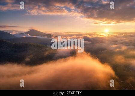 Berge in Wolken bei Sonnenaufgang im Sommer. Luftaufnahme Stockfoto