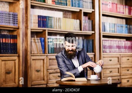 Lachen, Entspannen, Vergnügen, Freizeit, Hobby-Konzept. Happy man sitzt im Vintage-Interieur und genießt entspanntes Lesen. Bärtiger Mann in formeller Kleidung besucht Bibliothek. Reifer Mann mit lächelndem Gesicht hat Tee. Stockfoto