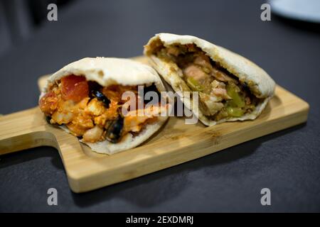 Zwei leckere Pita-Sandwiches. Einer davon mit Feta-Käse, schwarzen Oliven, Tomaten und Huhn, der andere mit Lachs und Gurken Stockfoto