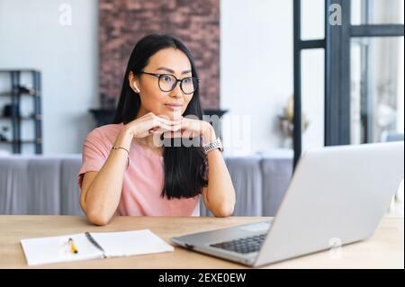 Fokussierte schöne asiatische starrte auf dem Laptop-Bildschirm sitzen am Schreibtisch im modernen Home Office, Webinar, Lesen und Recourching Stockfoto