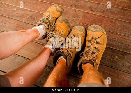 Eine kaukasische Frau und Männer Füße in sehr schmutzigen Wanderstiefeln mit rot orangefarbenem Schmutz gesehen. Stockfoto