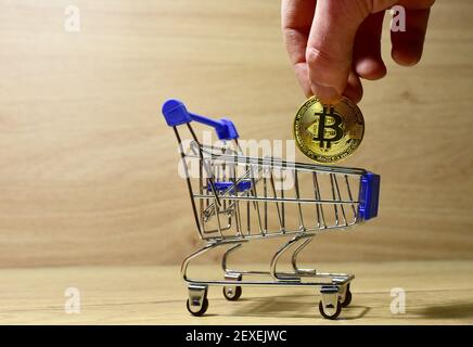 Bitcoin im Warenkorb. Man's Hand legt eine BTC Gold Krypto-Münze in Mini-Shopping-Trolley. Blockchain und Finanztechnologie. Kauf von Waren und Lebensmitteln Stockfoto