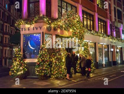 Das Ivy Restaurant in London in der Nacht mit Buntglasfenstern und Weihnachtsbeleuchtung und Kunden warten darauf, nach innen zu gehen. Stockfoto