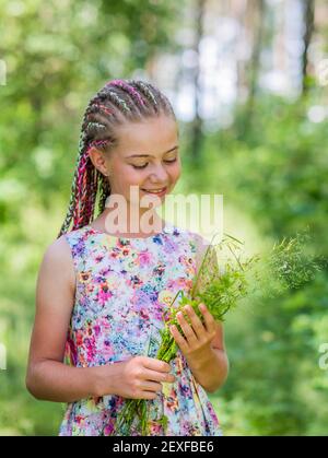 Ein junges Mädchen mit farbigen Dreadlocks hält an einem Sommertag Blumen in den Händen. Stockfoto