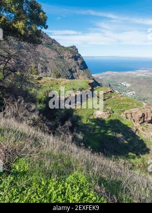 Blick auf Klippen und felsige atlantikküste im Nordwesten von Gran Canaria mit Blick auf die Stadt Agaete, Serpentinenstraße und grüne Hügel. Kanarische Inseln Stockfoto