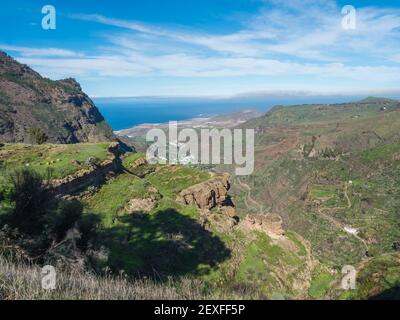 Blick auf Klippen und felsige atlantikküste im Nordwesten von Gran Canaria mit Blick auf die Stadt Agaete, Serpentinenstraße und grüne Hügel. Kanarische Inseln Stockfoto