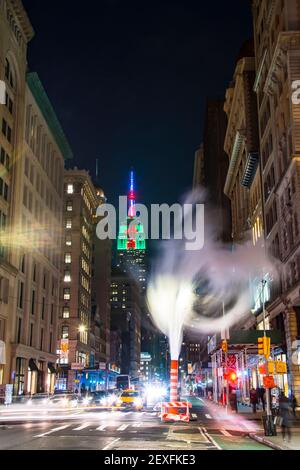 Das Empire State Building leuchtet während der Weihnachtsfeiertage in New York City unter den Gebäuden von Midtown Manhattan. Stockfoto