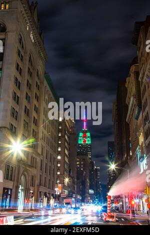 Das Empire State Building leuchtet während der Weihnachtsfeiertage in New York City unter den Gebäuden von Midtown Manhattan. Stockfoto