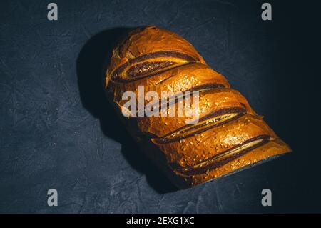 Ungewöhnlicher zweifarbiger frischer Laib Brot auf schwarzem Hintergrund, Foto in einer niedrigen Taste bei hartem Licht, Nahaufnahme Stockfoto