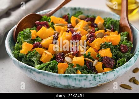 Herbstsalat mit Grünkohl, geröstetem Kürbis, Samen und getrockneten Preiselbeeren in einer Schüssel. Grauer Hintergrund. Modell. Draufsicht. Stockfoto