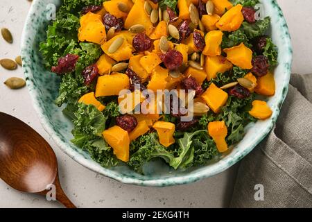 Herbstsalat mit Grünkohl, geröstetem Kürbis, Samen und getrockneten Preiselbeeren in einer Schüssel. Grauer Hintergrund. Modell. Draufsicht. Stockfoto