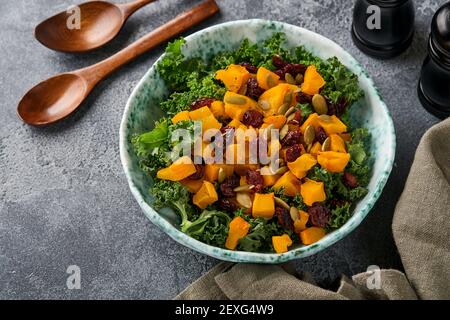 Herbstsalat mit Grünkohl, geröstetem Kürbis, Samen und getrockneten Preiselbeeren in einer Schüssel. Grauer Hintergrund. Modell. Draufsicht. Stockfoto