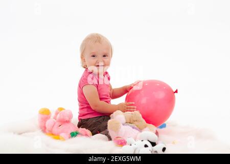 Ein kleines Mädchen in rosa Kleidung spielt auf dem Boden mit Spielzeug Stockfoto