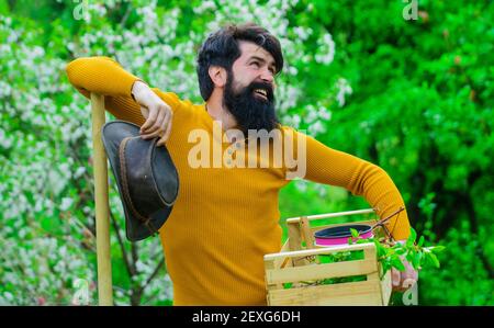 Frühjahrsfarmen. Gartenarbeit. Lächelnder Gärtner oder Landwirt mit Schachtel Gartengeräten. Bärtiger Mann, der im Garten arbeitet. Stockfoto