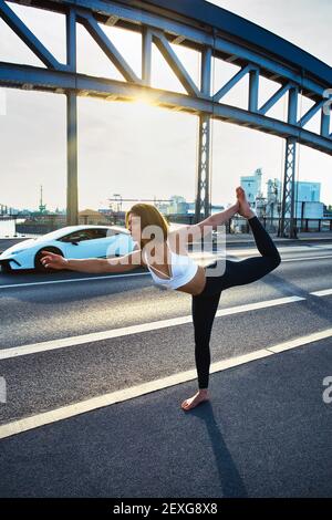 Junge Frau, die an sonnigen Tagen Yoga auf der Straße in Frankfurt am Main, Hessen, Deutschland, durchführt. Stockfoto
