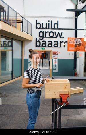 Hübsche junge Tischlerin, die die Holzoberfläche aus Holz formt Kiste im städtischen Produktionsraum Tatcraft in Frankfurt, Deutschland Stockfoto