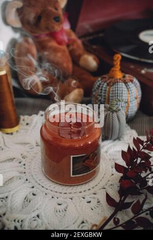 Winter Gemütliches Stimmungskonzept. Stillleben Details in der häuslichen Einrichtung des Wohnzimmers. Duftsoja Aromatherapie Kerze und Tasse Tee mit Dampf auf dem Tisch. Gemütlich Stockfoto