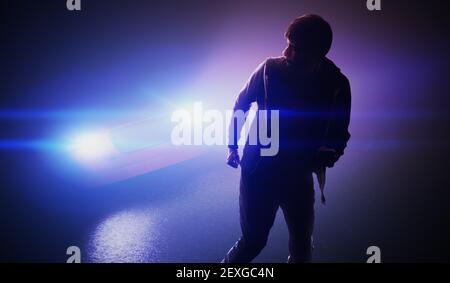 Silhouette eines Mannes, der nachts auf der Straße vom Auto wegläuft. Stockfoto
