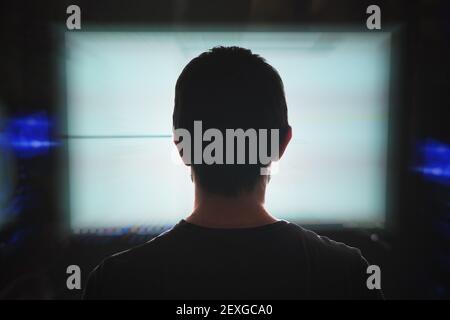 Junger Programmierer schaut auf Computerbildschirm in der Nacht. Blick von hinten. Stockfoto