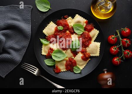 Leckere italienische Ravioli mit Tomatensauce und Basilikum auf dunklem Teller serviert. Stockfoto
