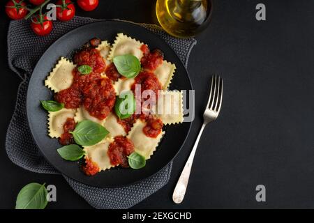 Leckere italienische Ravioli mit Tomatensauce und Basilikum auf dunklem Teller serviert. Stockfoto