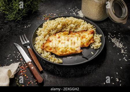 Gegrilltes hawaiianisches Huhn mit Käse, Ananas und gekochtem Reis auf einem schwarzen Teller serviert Stockfoto