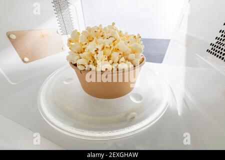 Fertig Popcorn in der Mikrowelle. Salziger Snack, zubereitet im Küchengerät. Heller Hintergrund. Stockfoto