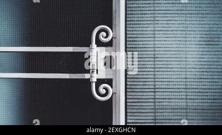 Eine Nahaufnahme Textur eines Gebäudes Eingang mit der Tür und das Fenster sowohl mit verstärktem Glas und einem schäbigen schmiedeeisernen Türknopf mit Locken, Farbe Stockfoto