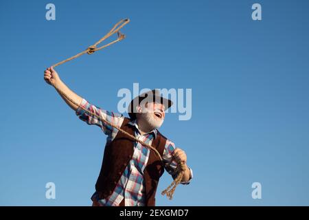 Lasso werfen. Alter Wilder Westen Cowboy mit Seil. Bärtiger Westernmann mit brauner Jacke und Hut, der Pferd oder Kuh fängt. Stockfoto