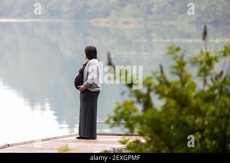 Nicht erkennbare schwangere Frau auf Pier in der Nähe des Sees halten Bauch Stockfoto