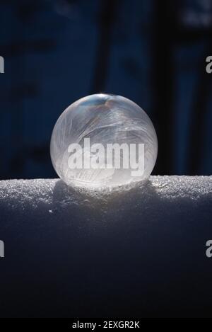 Nahaufnahme der gefrorenen Seifenblase auf dem Schnee mit dunklem Hintergrund. Stockfoto