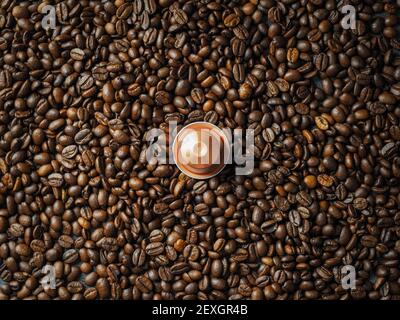 Eine goldene, recycelbare italienische Espresso-Kapsel auf einem Stapel gerösteter Kaffeebohnen. Overhead-Ansicht. Stockfoto