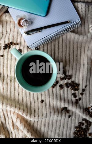 tasse Kaffee neben Notebook mit Handy und Stift darauf Stockfoto