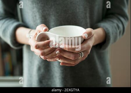 Nahaufnahme einer Frau in warmer Strickmode, Hände mit einem weißen Becher. Entspannte, gemütliche Atmosphäre, Home Lounging Lifestyle-Konzept Stockfoto