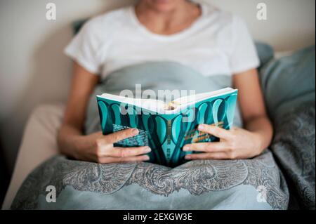 30s junge Erwachsene kaukasische Frau mit einem Buch Lesung im Bett. Indoor Wochenende Lifestyle, Home Lounging Konzept Stockfoto