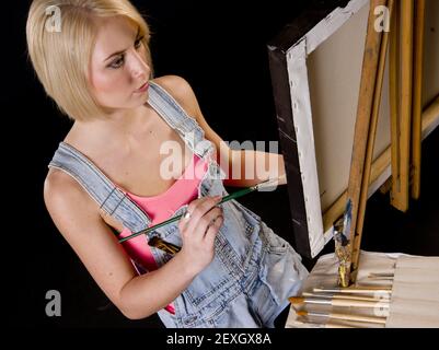 Happy Blonde Woman bietet Finishing Touches to Painting on Easel Stockfoto