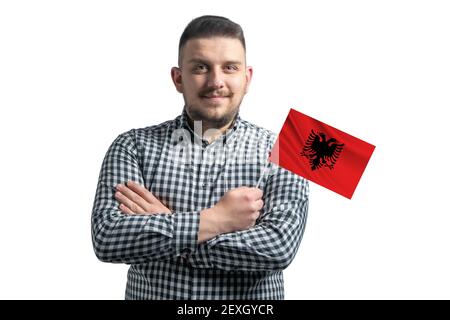 Weißer Kerl hält eine Flagge von Albanien lächelnd zuversichtlich mit gekreuzten Armen auf einem weißen Hintergrund isoliert. Stockfoto