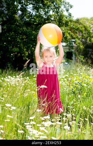 Nettes kleines Mädchen mit einem Ball auf einer Sommerwiese Stockfoto