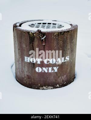 Nahaufnahme eines heißen Kohlebehälters mit einem weißen Text „nur heiße Kohle“ in einem verschneiten Feld Stockfoto