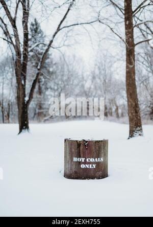 Eine vertikale Aufnahme eines heißen Kohlebehälters mit einem Weißer Text „nur heiße Kohlen“ in einem schneebedeckten Feld Stockfoto