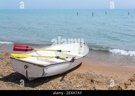 Weißes Ruderboot mit gelben und roten Rudern auf dem Pebbley Ufer, während sie von der Brandung wie es geläppt Blick auf den fernen Horizont des Lake Mi Stockfoto