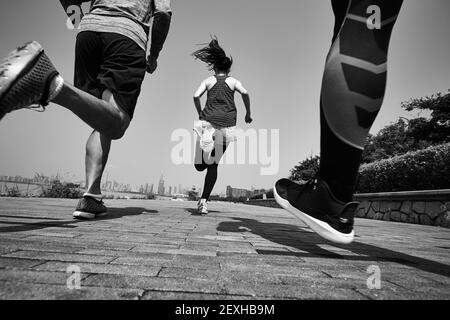 Drei junge asiatische Erwachsene joggen im Freien, hinten und in den tiefen Winkeln, schwarz und weiß Stockfoto