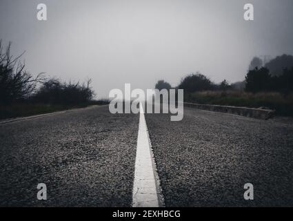Ein flacher Fokus von weißer Farbe auf der rauen Oberfläche Asphaltstraße an einem nebligen Morgen Stockfoto