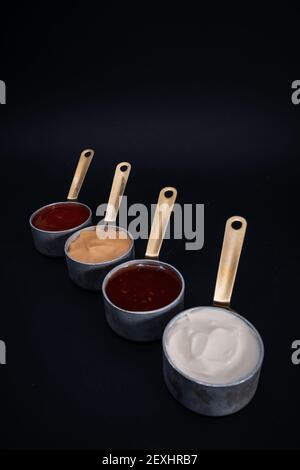 Eine vertikale Aufnahme von kleinen Pfannen mit verschiedenen Saucen auf Schwarzer Hintergrund Stockfoto